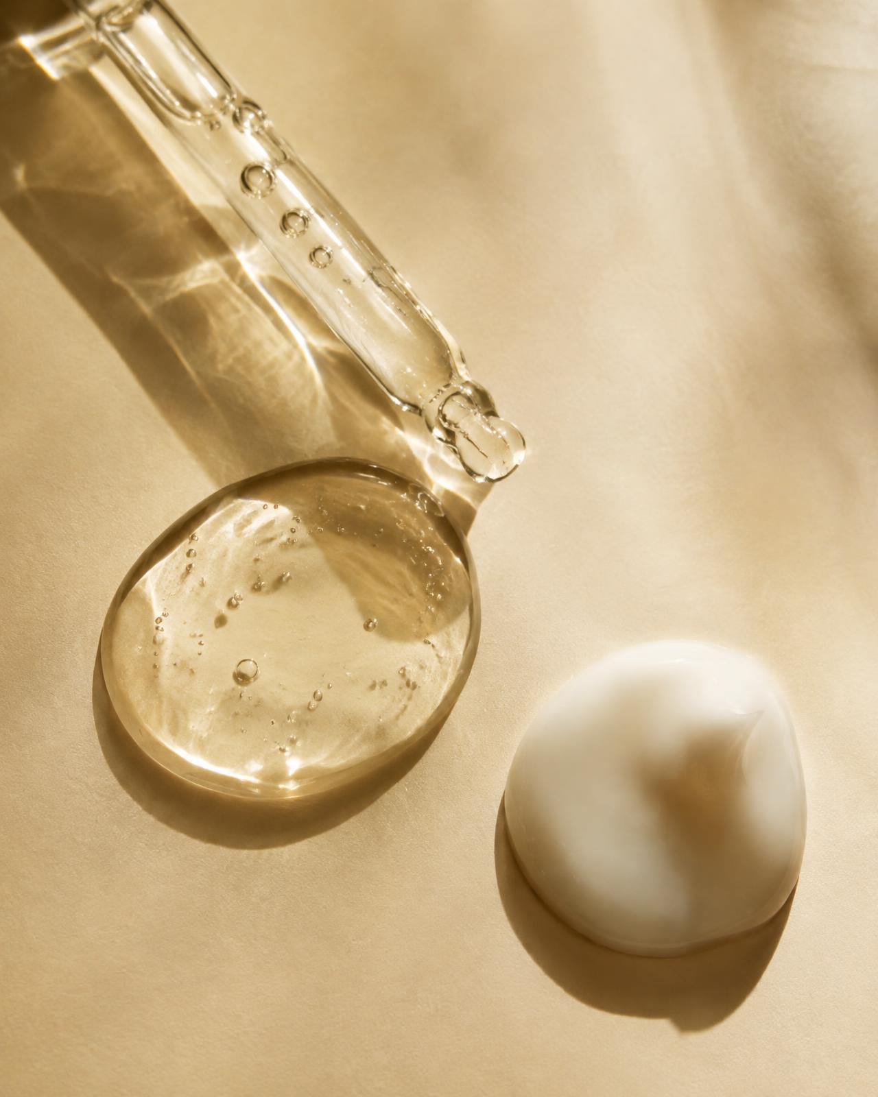 Translucent gel and white lotion droplets in warm sunlight with a glass dropper